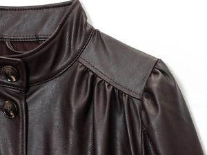 Macro detail of dark brown leather jacket with stand collar and amber textured buttons