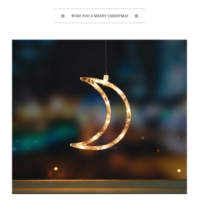 Close-up of crescent moon LED hanging light with warm yellow glow against bokeh city night
