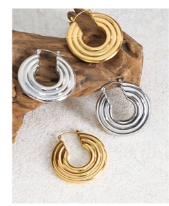 Detail of chunky triple-ribbed hoop earrings in gold and silver finish on wood