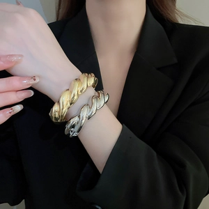 Detail von gedrehten Armreifen in Gold und Silber am Handgelenk eines Models