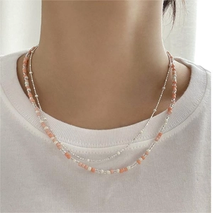 Detail of minimalist double-layered beaded necklace with orange and white beads on a model