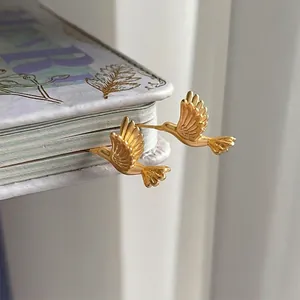 Artistic matte gold hummingbird studs displayed inside a vintage book page for women