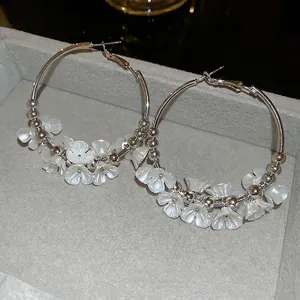 Silver metal hoop earrings featuring white acrylic flower petals on a grey velvet tray
