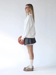 Dettaglio di una felpa bianca oversize con gonna a pieghe grigia e accessorio da basket