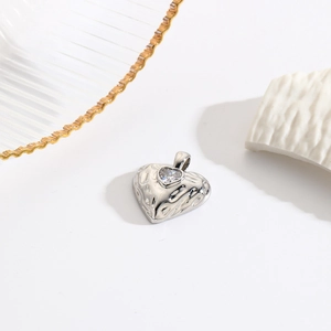 Macro shot of silver heart pendant featuring a textured surface and center zircon stone