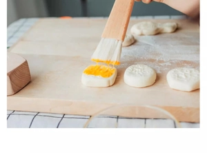 Détail d'un pinceau en hêtre appliquant de la dorure sur une pâtisserie ronde et lisse