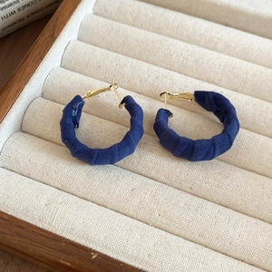 Close-up of navy blue velvet C-shaped hoop earrings with gold metal on a beige tray
