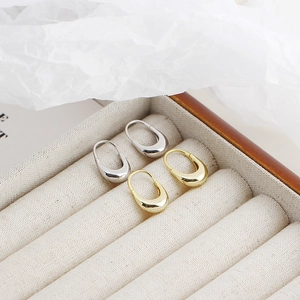 Close-up of minimalist U-shaped silver and gold hoop earrings on a beige jewelry box