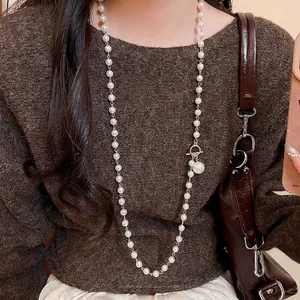 Collier en perles élégant avec boucle OT dorée et pendentif goutte sur pull marron