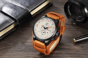 Detailed shot of a CURREN brown leather watch on a vintage wood desk with props