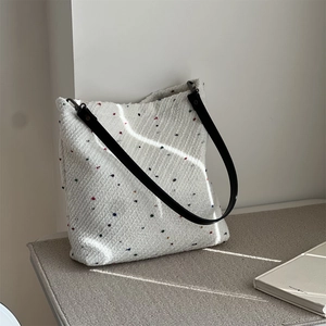 Close-up of white woven tote bag featuring colorful dots and black leather shoulder strap