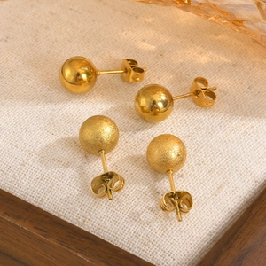 Close-up of polished and frosted gold stainless steel ball earrings on fabric background