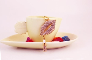 Macro detail of rhinestone lips keychain with mini lipstick charm on a ceramic cup