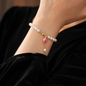 Detailed view of pearl bracelet with pink dragon fruit charm worn on a wrist
