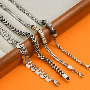 Men's stainless steel Cuban and box chain bracelets with gold accents on wood stand