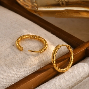 Macro detail of gold-plated hoop earrings with cross-hatch diamond pattern and clasp