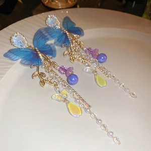 Macro shot of long fringe earrings with blue mesh butterfly and golden leaf tassels