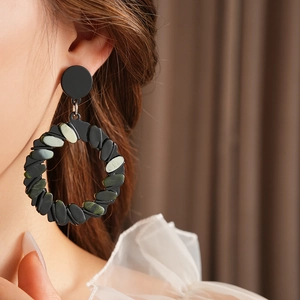 Close-up of model wearing large black hoop earrings with green resin inlay detail