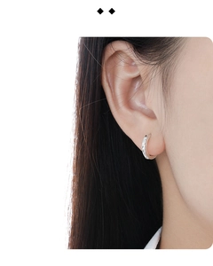 Close-up of minimalist silver hoop earrings with intricate floral engraved texture on ear
