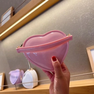Pink heart-shaped jelly handbag with gold chain held by a hand in a boutique setting