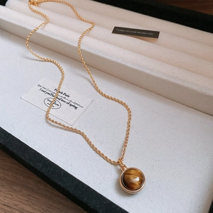 Detail of gold-plated rope chain necklace with a round tiger eye stone pendant