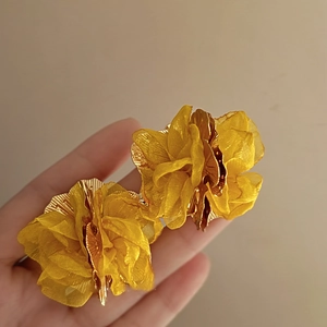 Detail of yellow flower earring featuring chiffon fabric petals and a golden metal base