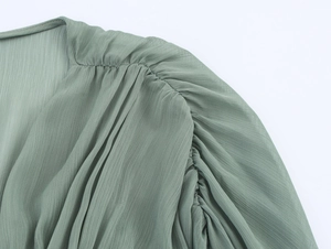Detailansicht eines hellgrünen Chiffonkleids mit Plissee an Schulter und Fledermausärmel