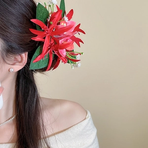 Detail of vibrant red fabric flower hair clip with green leaves on long straight hair