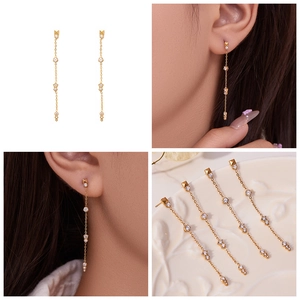 Détail de boucles d'oreilles pendantes dorées avec zircons montrant l'effet porté élégant