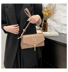 Detail view of beige crossbody bag with gold SS logo and elegant tassel hanging pendant