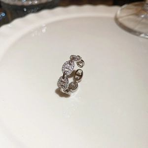 Close-up of silver chain link ring with zircon stones on a white ceramic tray