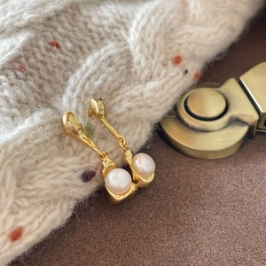 Elegant gold drop earrings with round white pearls on minimalist knitted sweater background