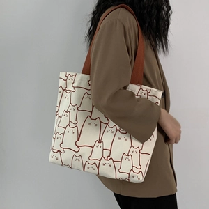Detail of a large cream canvas tote bag with brown cat print patterns on model