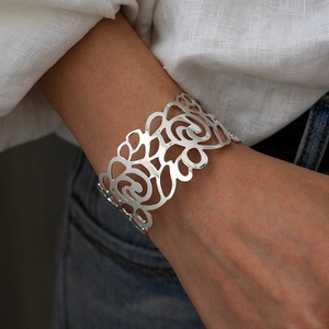 Close-up of wide cuff bracelet featuring intricate floral cutout patterns on model