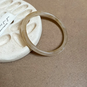 Detail of translucent amber resin bangle displayed on a textured white ceramic plate