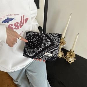 Detail of floral paisley canvas pouch held by hand featuring black pattern and logo