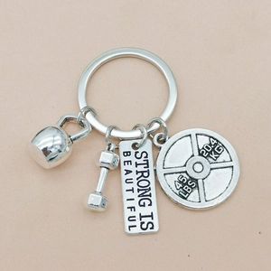 Detail of silver fitness keychain with kettlebell, dumbbell and Strong Is Beautiful tag