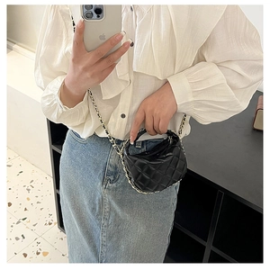 Detail of mini black quilted bag with gold chain strap on a white shirt and denim outfit