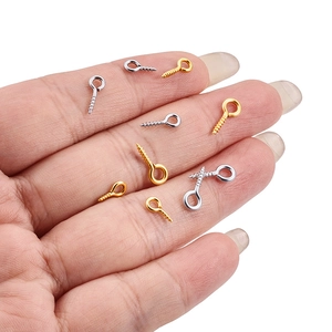 Macro shot of tiny gold and silver screw eye pins held in palm for size scale detail
