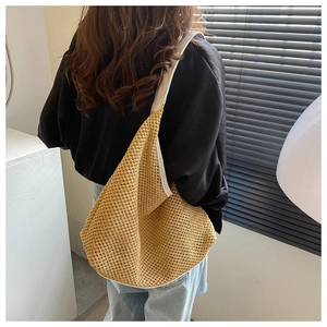 Shoulder shot of a khaki woven straw beach bag with white strap and mesh texture detail