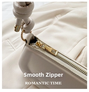 Detail of smooth gold zipper and knotted strap on a beige faux leather saddle bag
