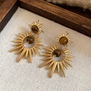 Detailed close-up of golden starburst drop earrings with brown stone and small zircons