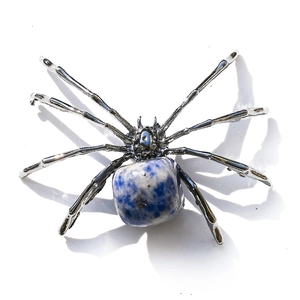 Macro detail of a silver spider ornament with natural blue and white stone on white background