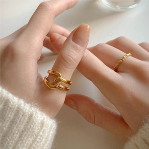 Close-up of minimalist gold cross rings and chain band worn on a hand with white knitwear