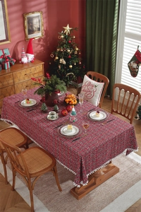 Close-up of red and green plaid tablecloth with white pom-pom tassels in a festive setting