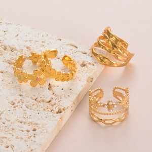 Detailed view of three gold-plated rings with flower, wave, and pearl accents on stone