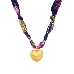 Detail of gold heart pendant with navy blue floral silk ribbon on white background