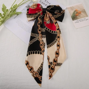 Close-up of printed satin bow hair clip with long ribbons and golden chain pattern