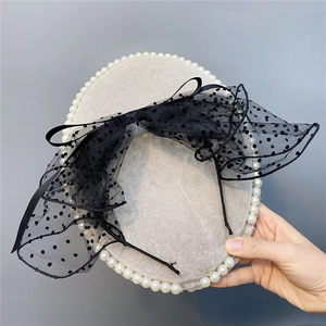 Detail of a black polka dot lace bow headband with delicate mesh texture and pearls