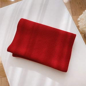 Detailed close-up of folded red knitted scarf on a wooden surface with soft shadows